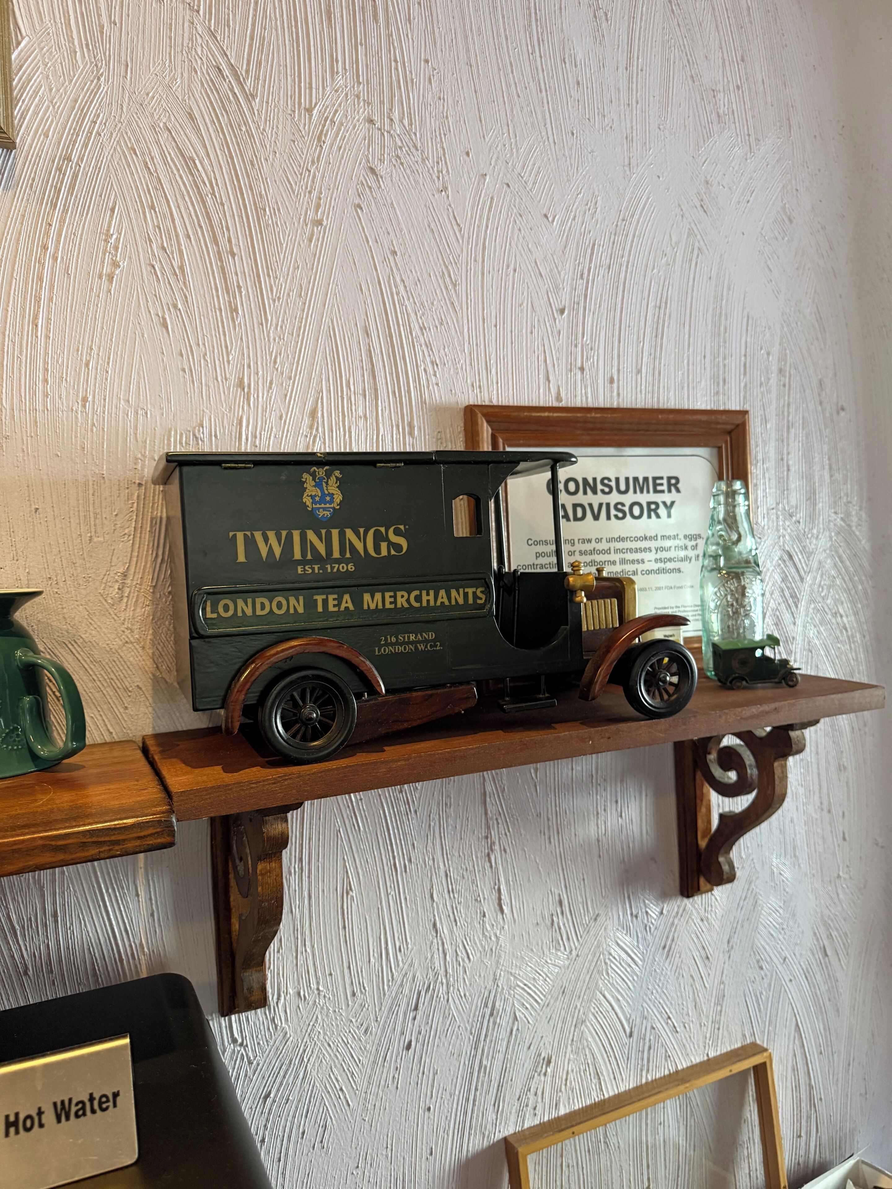 Ein Modell eines alten Tee-Lieferwagens mit der Aufschrift 'TWININGS LONDON TEA MERCHANTS', platziert auf einem Holzregal.