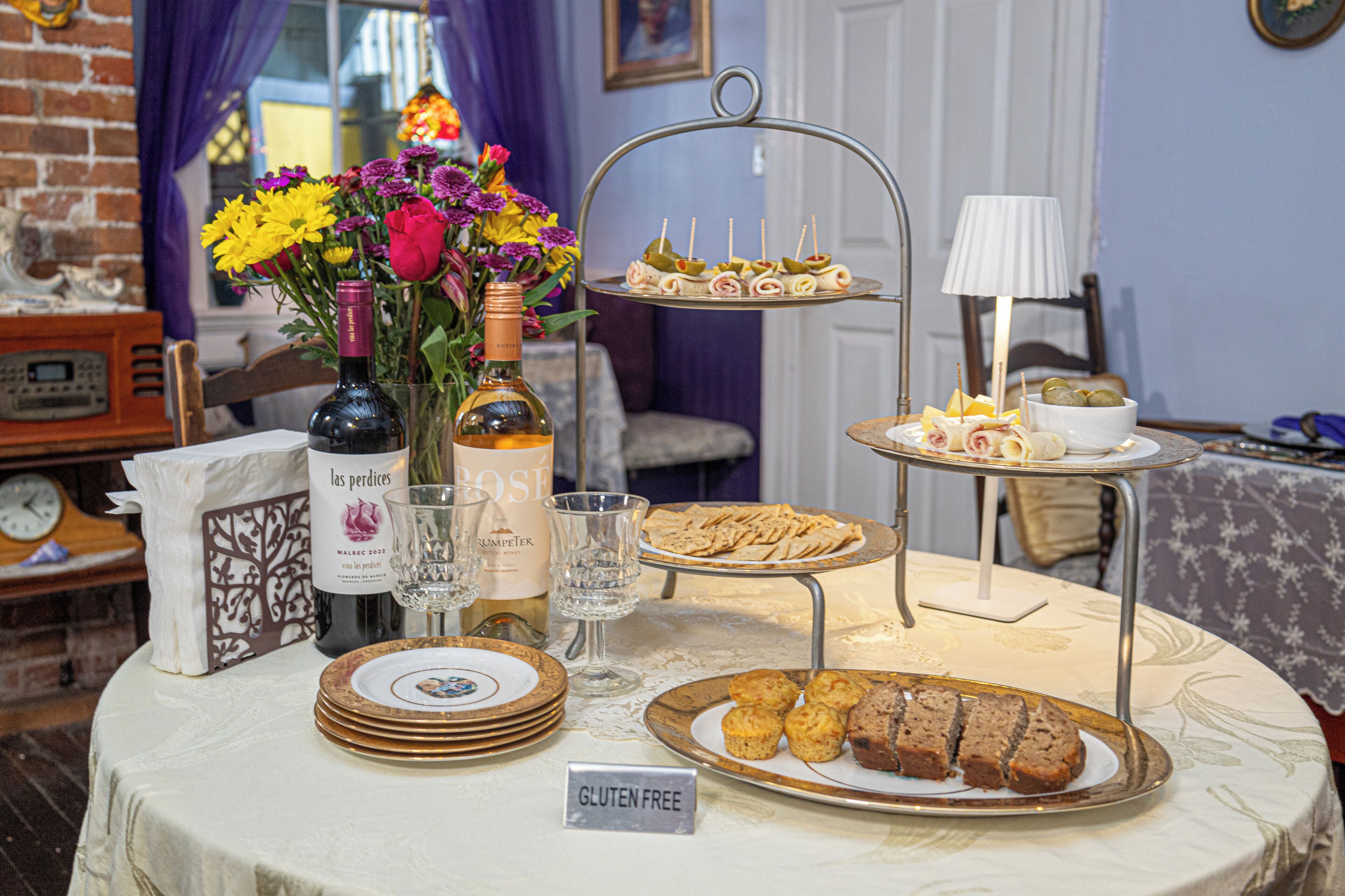 Une table dressée avec des bouteilles de vin, des verres, un panneau indiquant « sans gluten » et diverses pâtisseries.