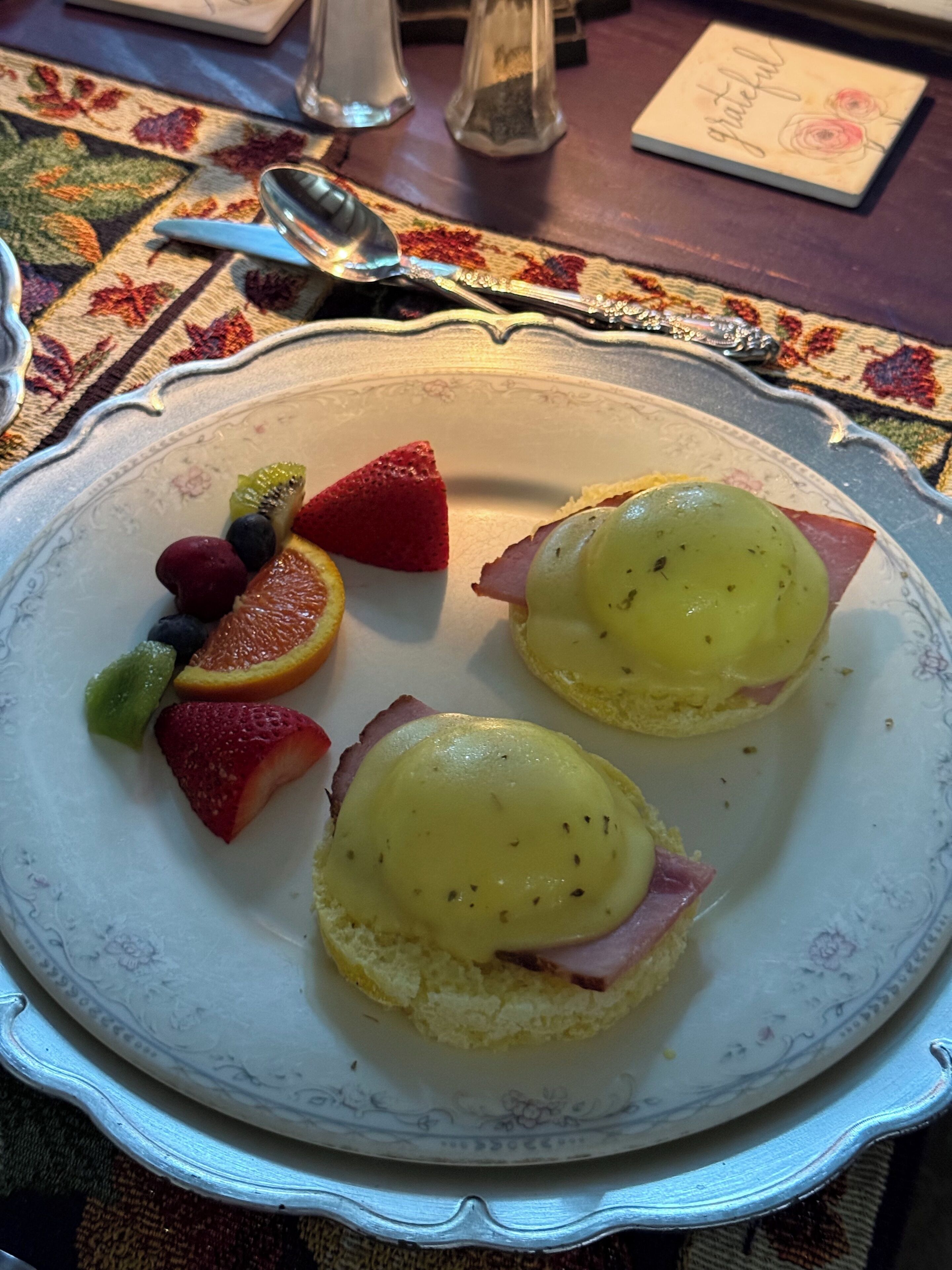 A plate with two eggs benedict sandwiches, accompanied by a variety of fresh fruits.