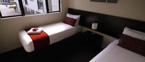 A hotel room with two beds, a window with a view of the street, and a nightstand with a lamp.