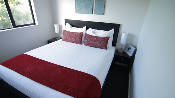 Ein Hotelzimmer mit einem großen Bett, zwei Nachttischen, einem Fenster und zwei an der Wand befestigten Kunstwerken.