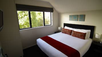 Une chambre d’hôtel avec un grand lit, deux tables de chevet, une fenêtre donnant sur la verdure et deux œuvres d’art accrochées au mur.