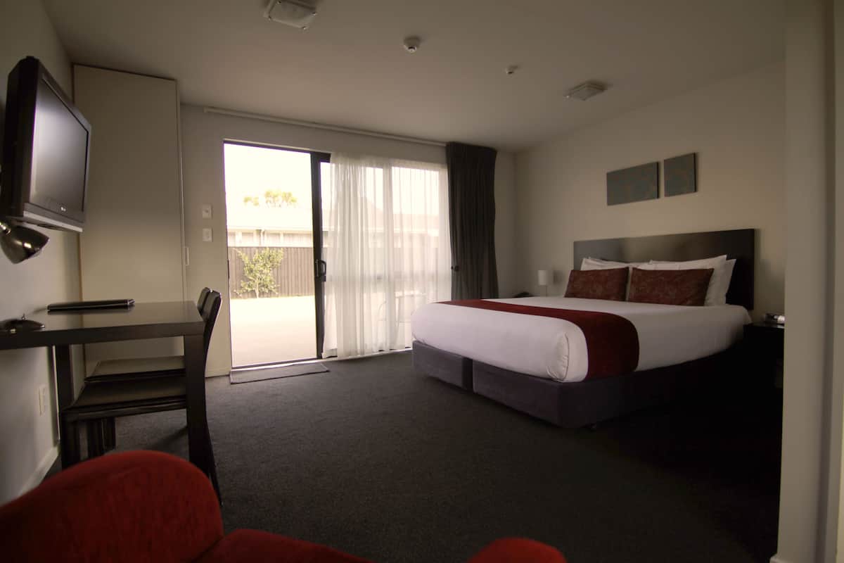 Ein Hotelzimmer mit einem Bett, einem Schreibtisch, einem Stuhl, einem Fernseher und einer Schiebetür.