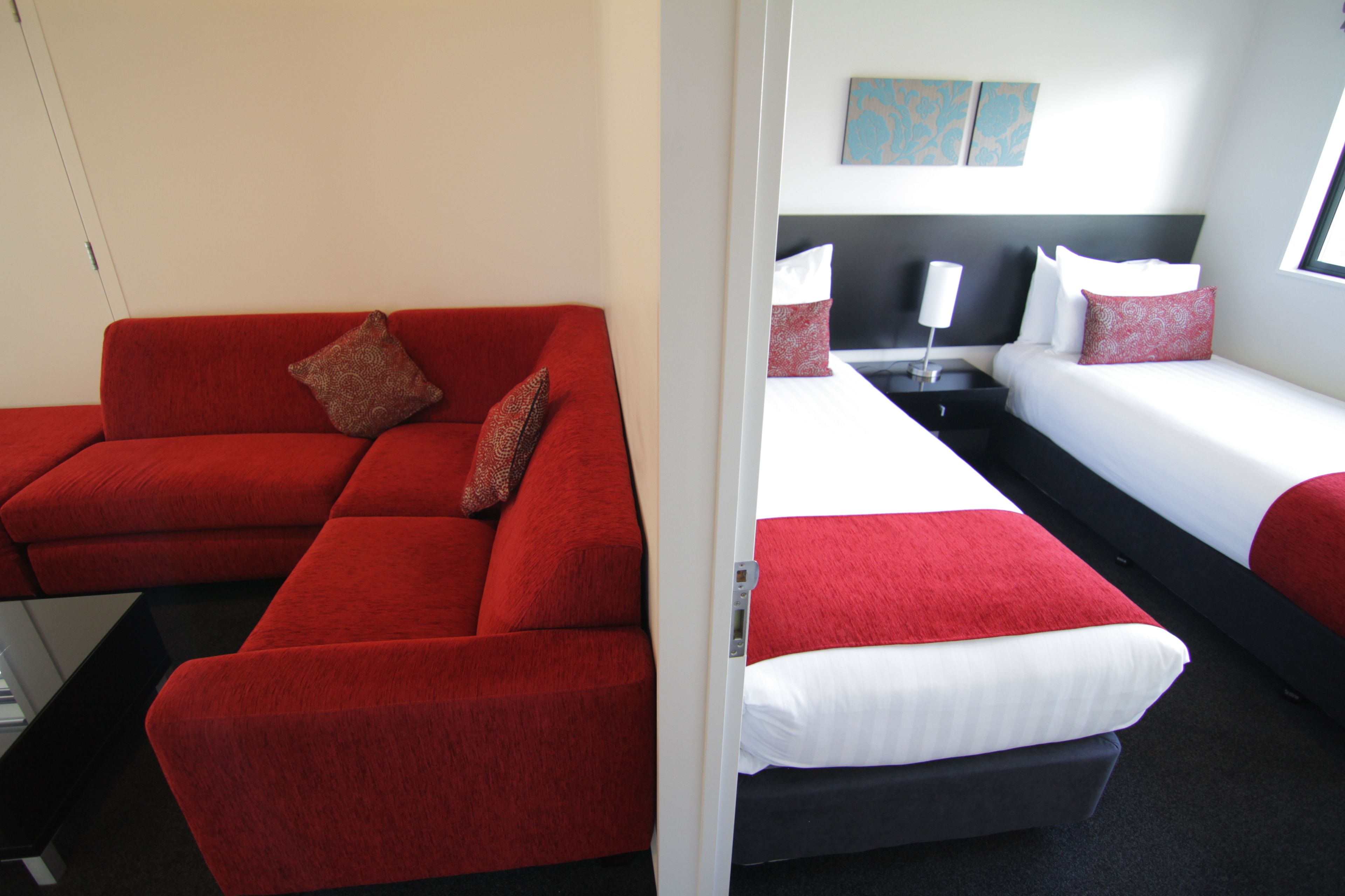 A hotel room with a red sofa, two single beds, a nightstand with a lamp, and a painting on the wall.