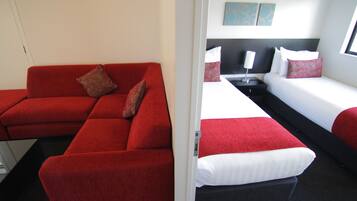A hotel room with a red sofa, two single beds, a nightstand with a lamp, and a painting on the wall.