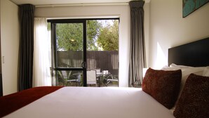 Ein Hotelzimmer mit einem großen Bett, Blick auf eine Terrasse mit Gartenmöbeln und einer Glastür.