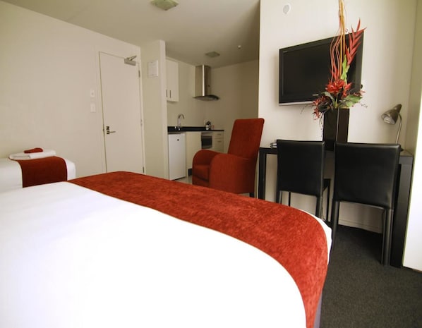 A hotel room with a large bed, a desk with two chairs, a small kitchenette, and a TV on the wall. - 175 Metropolitan Executive Motel on Riccarton (Christchurch)