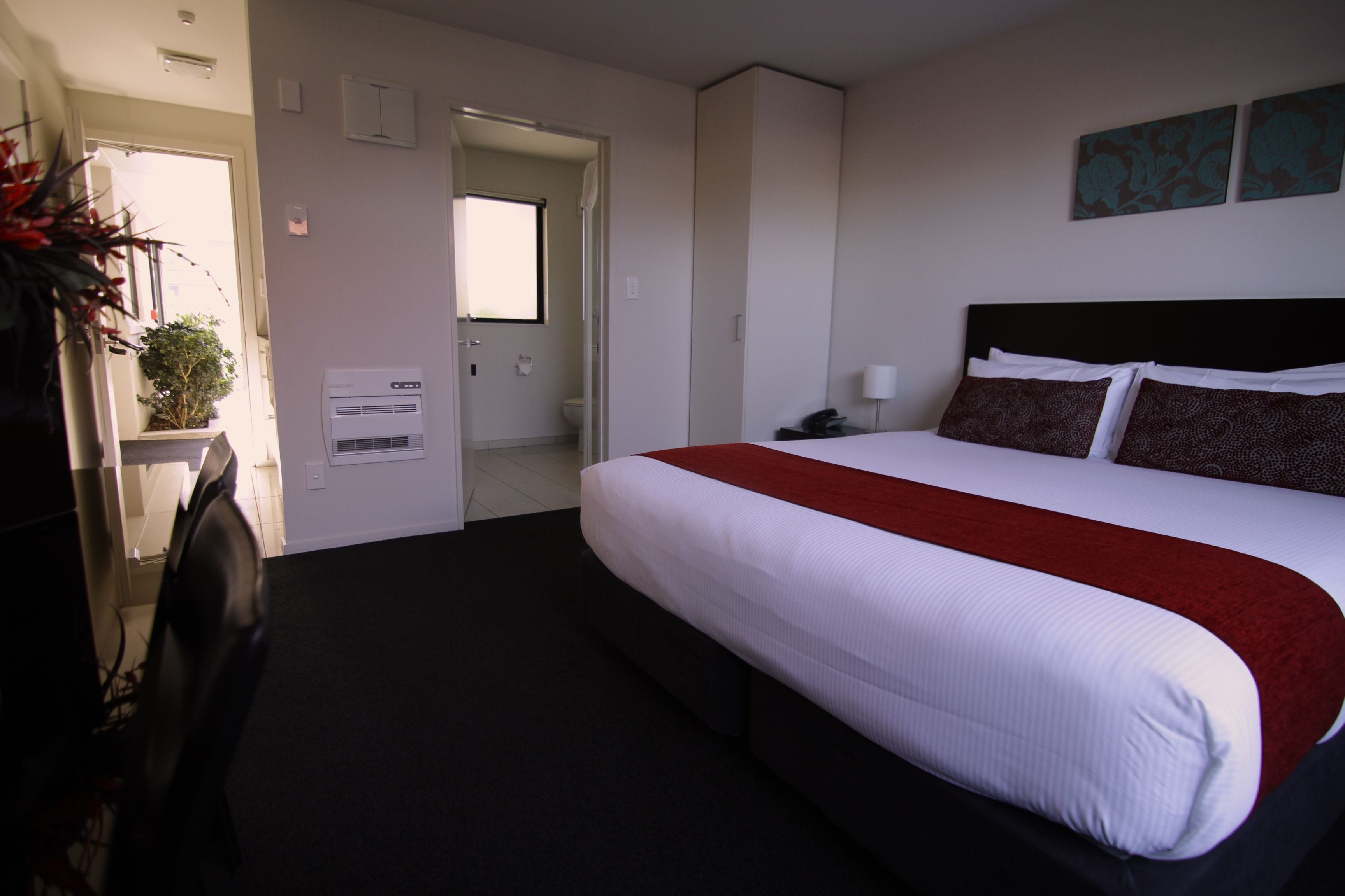 Une chambre d’hôtel avec un grand lit, un bureau et une chaise. On y trouve une porte donnant sur une salle de bain et une fenêtre.