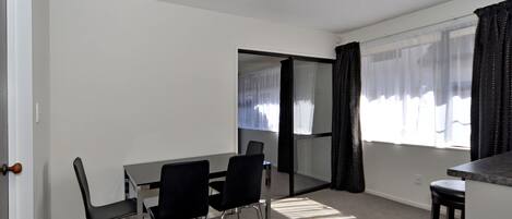 A room with a dining table, two chairs, a small kitchen area, and a sliding glass door leading to a balcony.