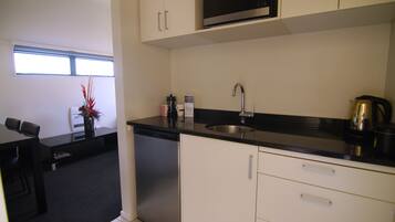 Een compacte keuken met witte kastjes, een zwart aanrecht en roestvrijstalen apparatuur, waaronder een magnetron en een koffiezetapparaat.