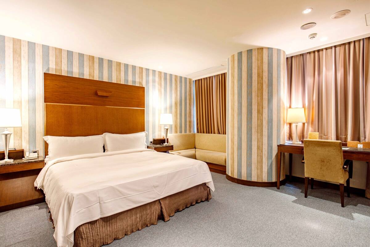 A hotel room with a large bed, a desk, a chair, and a sofa.