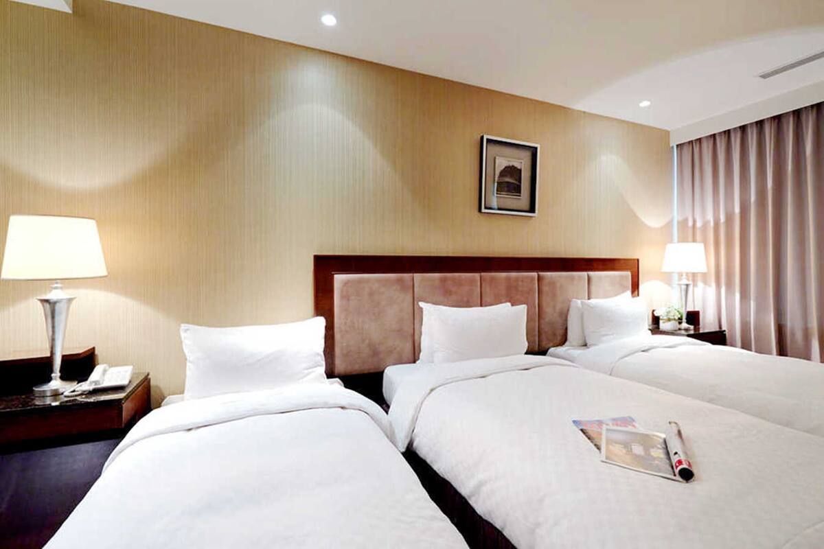 A hotel room with three beds, a wooden wall, a framed picture, and a window with curtains.
