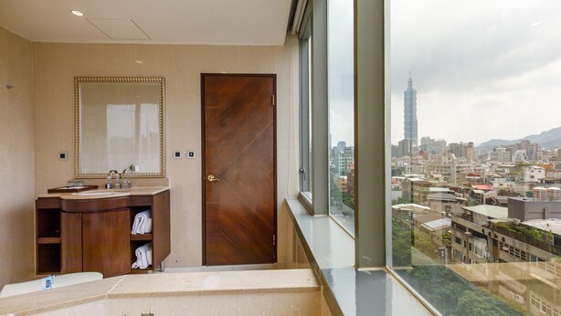 A modern bathroom with a large mirror, wooden door, and a view of a cityscape including a tall building. - Hotel HD Palace (Taipei)