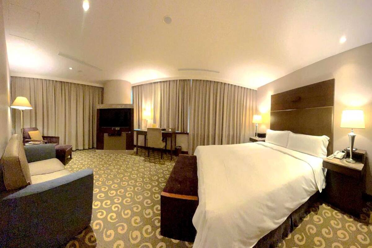 A hotel room with a large bed, a desk, a TV, and a seating area with a sofa and armchairs.