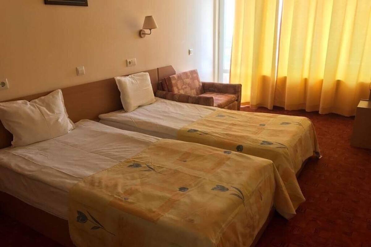 A hotel room with two single beds, a sofa, and a lamp.