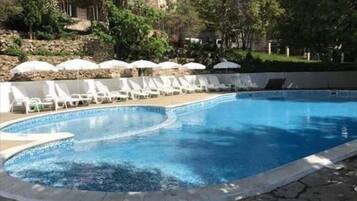 Ein Pool mit weißen Liegestühlen und Sonnenschirmen, umgeben von Bäumen und einem Gebäude im Hintergrund.