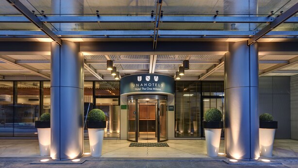 A modern hotel entrance with a revolving door, large pillars, and potted plants. - UNA Hotels The One Milano (San Donato Milanese)