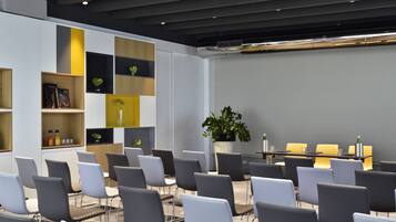 A modern conference room with a long table, grey chairs, and built-in shelving with books and decorative items.