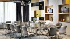 A modern conference room with a long table, grey chairs, and built-in shelving with books and decorative items. - UNA Hotels The One Milano (San Donato Milanese)