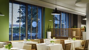 A restaurant with multiple tables set for dining, large windows with blinds, and a modern interior design. - UNA Hotels The One Milano (San Donato Milanese)