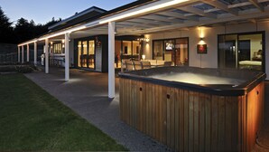 Un área moderna de hidromasaje al aire libre con un porche cubierto, una terraza de madera y un espacio interior bien iluminado.
