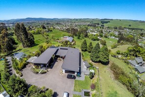 An aerial view of a residential area with a large two-story house featuring a garage, a driveway, and a well-maintained lawn. - City Lights Boutique Lodge (Rotorua)