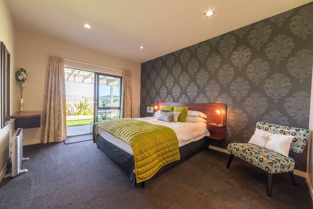 A bedroom with a bed, a chair, a desk, and a window with curtains.