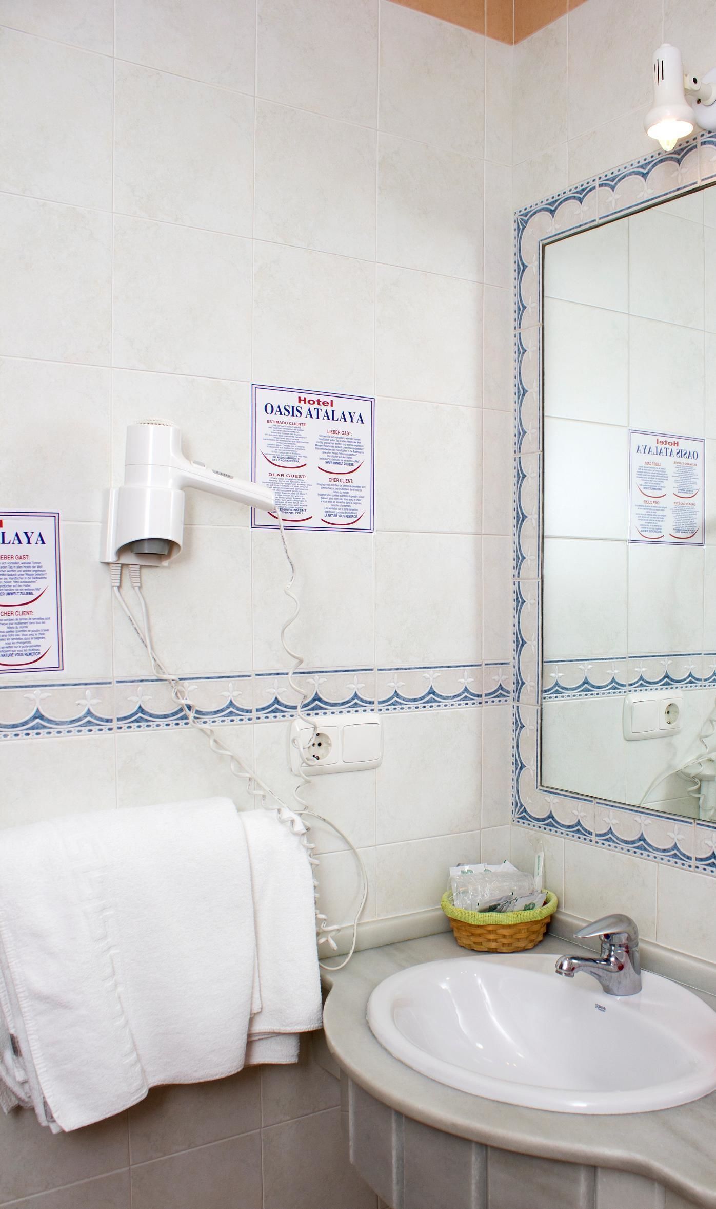 A bathroom with a white sink, a mirror with a decorative frame, a towel rack, and a hairdryer mounted on the wall.