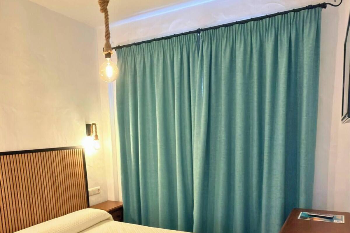 A hotel room with a bed, a wooden headboard, a nightstand, a lamp, and a curtain.