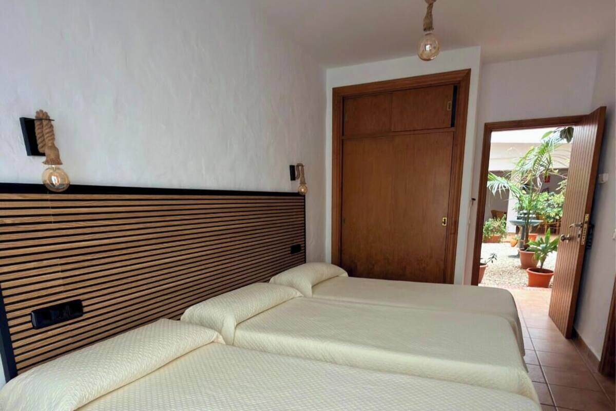 A room with a wooden headboard, a double bed, a wooden door, and a view of the outside.