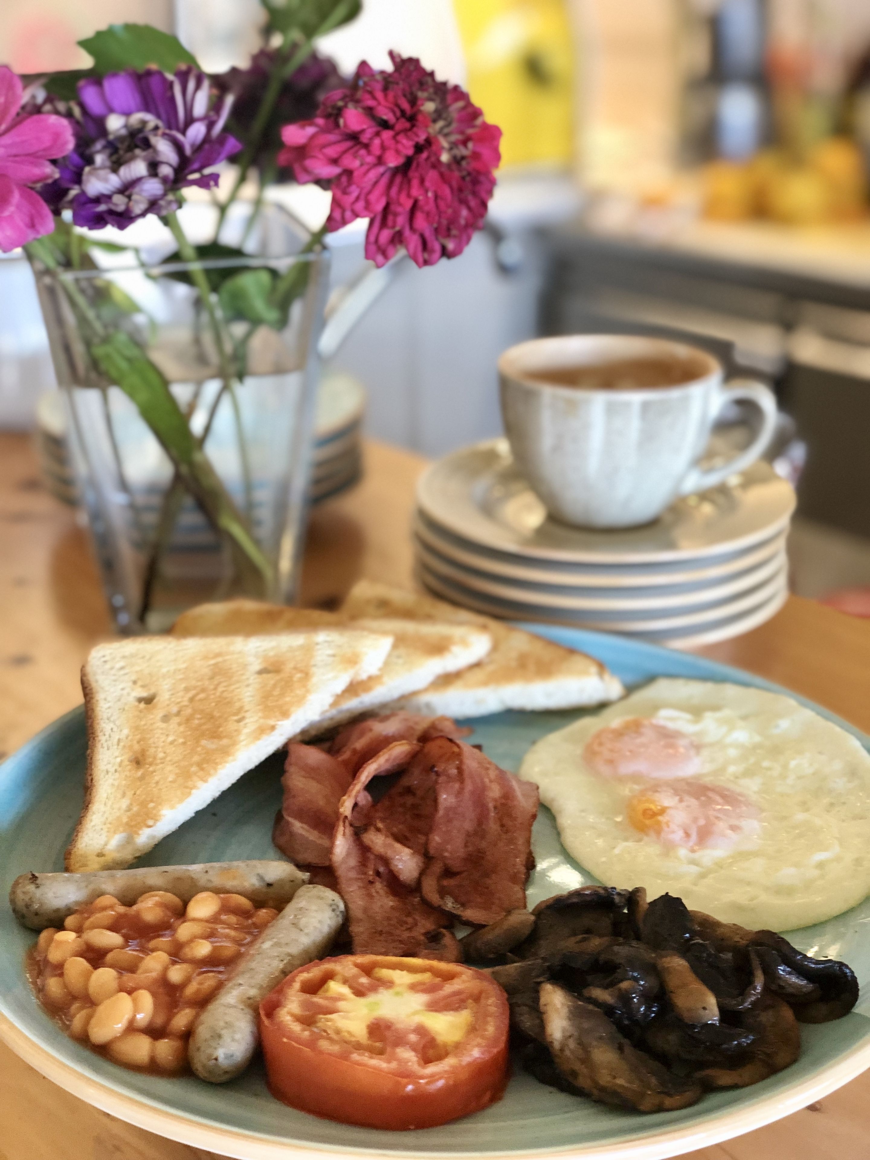 A breakfast plate with toast, bacon, eggs, beans, mushrooms, and a tomato.