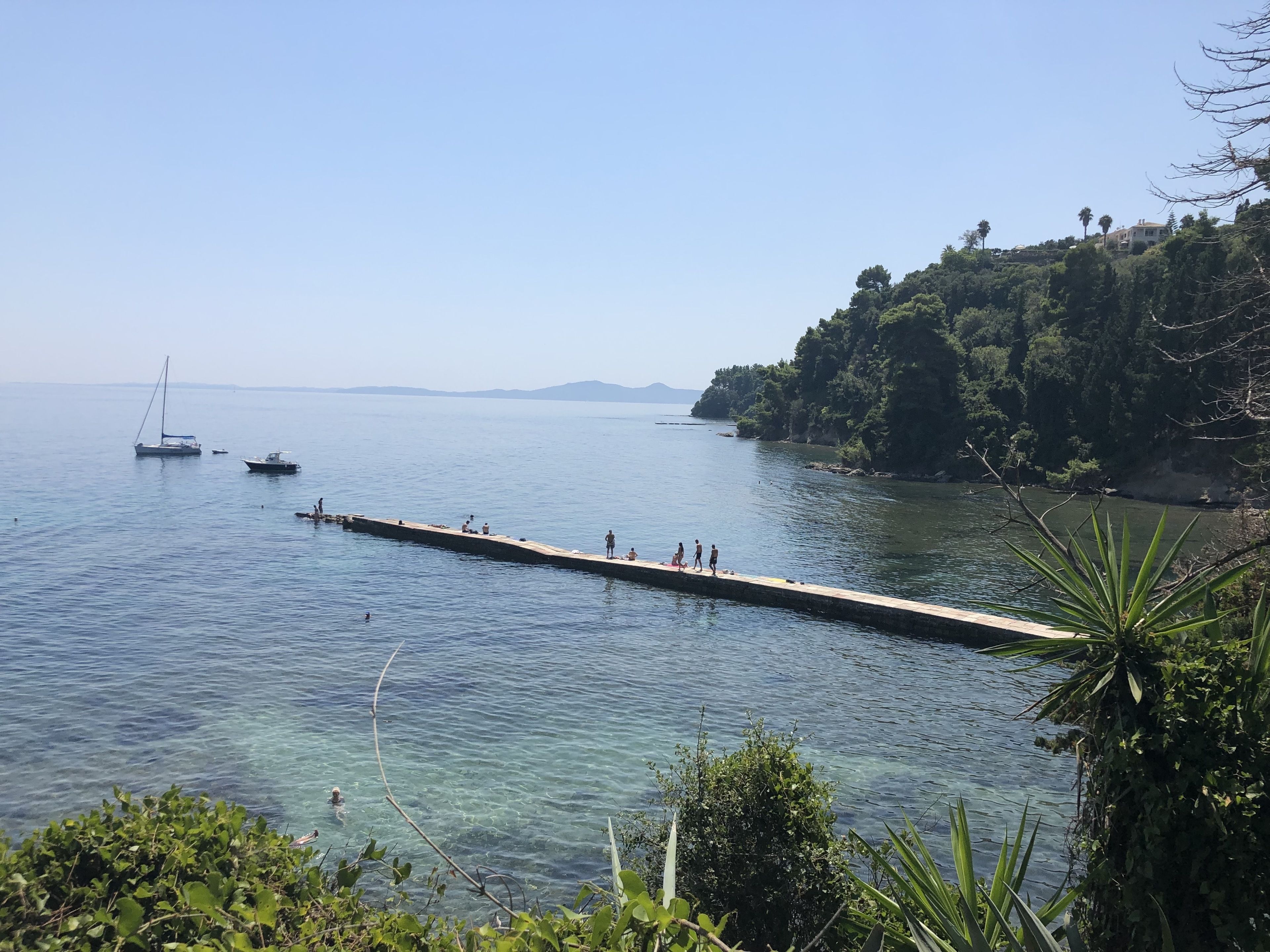 A pier extending into calm waters with boats and people.