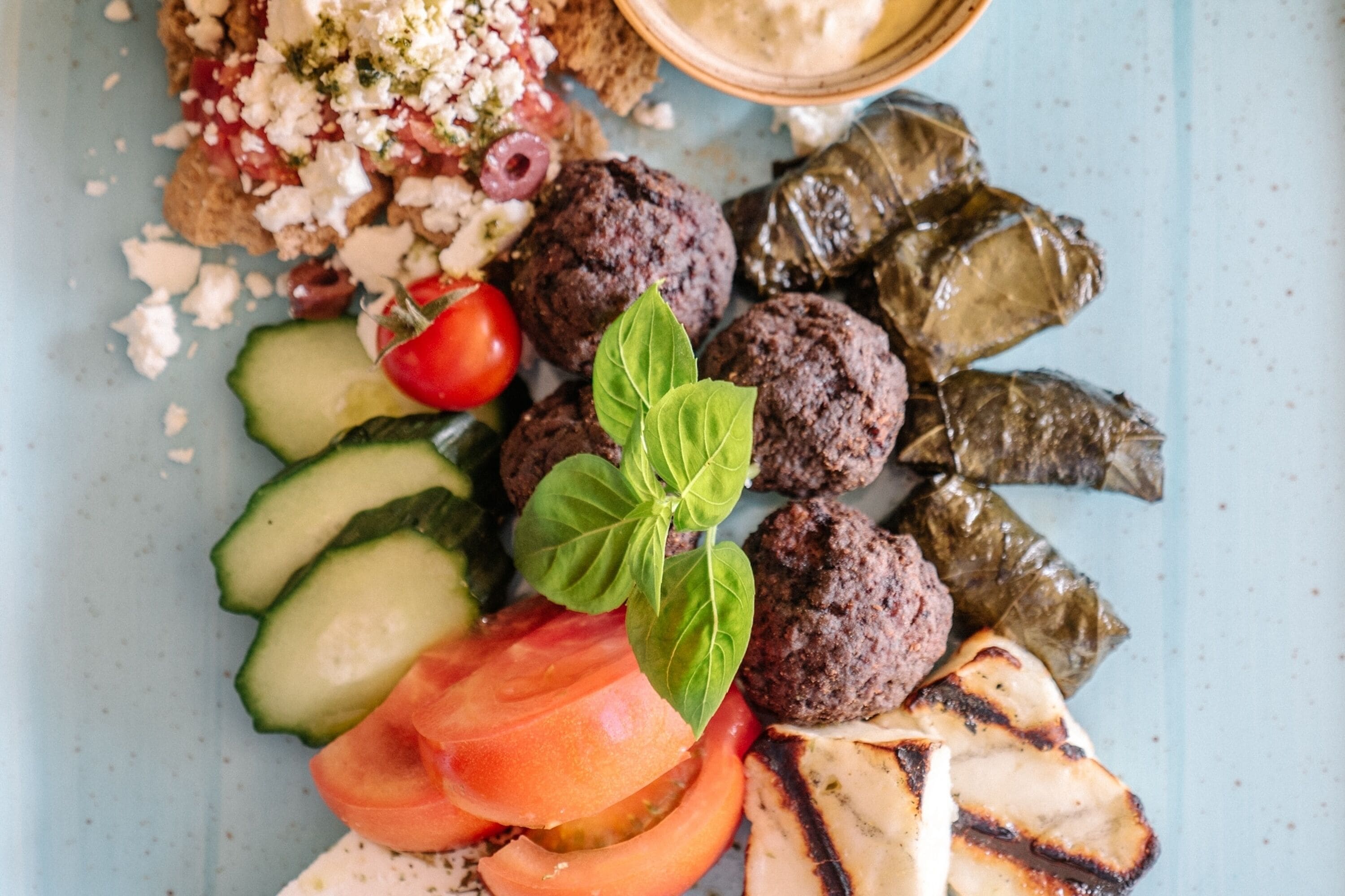 A plate with various foods including meatballs, stuffed grape leaves, grilled vegetables, and a small bowl of sauce.