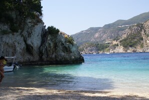 A coastal scene with clear turquoise water, rocky cliffs, and a boat docked near the shore. - Sebastians Family Hotel & Taverna (Corfu)