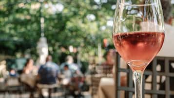 Una copa de vino tinto en una copa de martini, con un fondo desenfocado de personas y vegetación al aire libre.