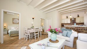 Un salón amplio con una mesa de comedor, muebles blancos, una mesa de centro con un jarrón de flores y una cocina al fondo.