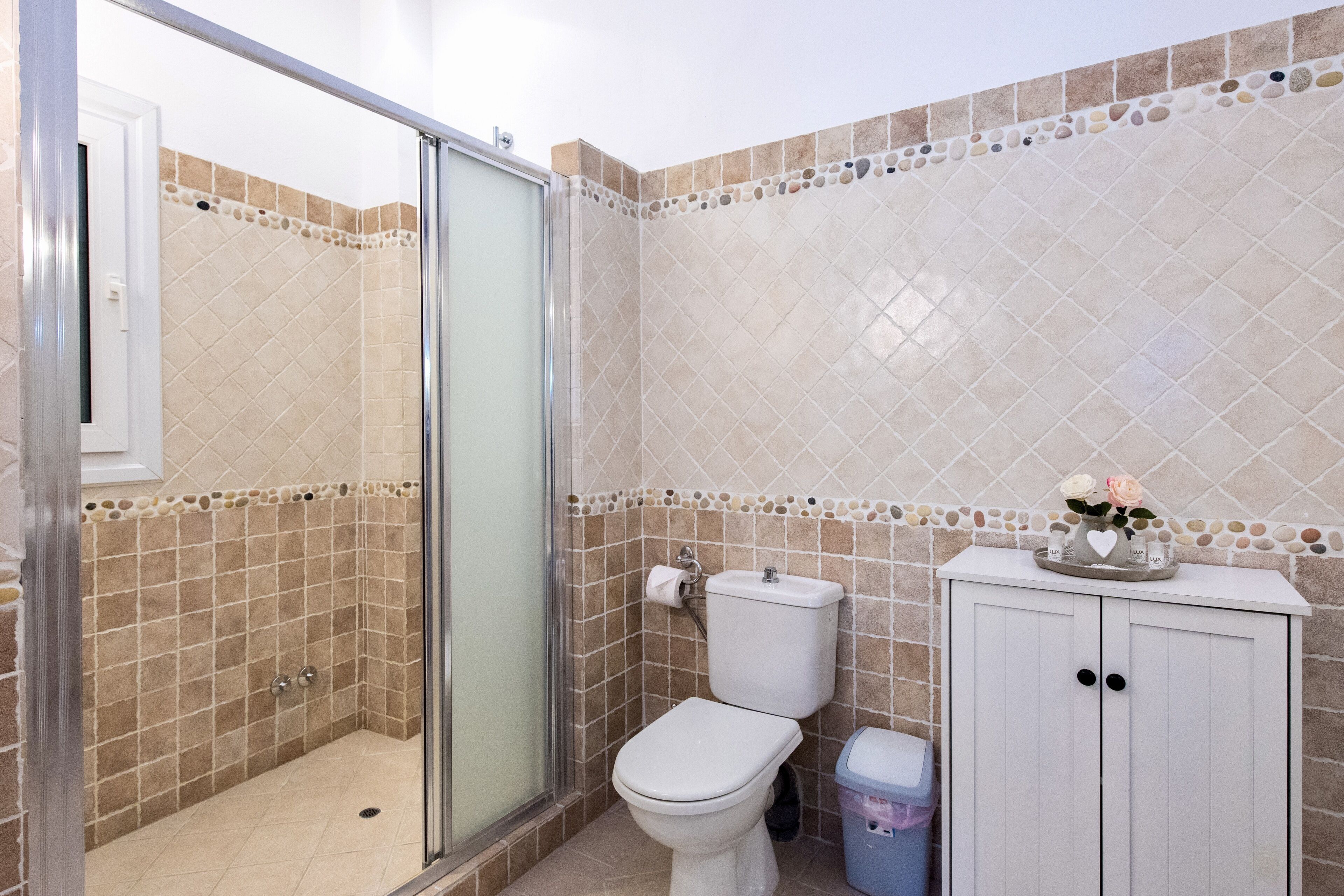Un baño con cabina de ducha de vidrio, inodoro y un mueble con un adorno encima.
