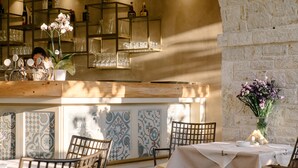 Interior de restaurante con barra, sillas, una mesa preparada para comer y un jarrón decorativo con flores.