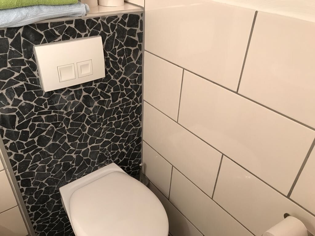 Ein Badezimmer mit Toilette, Wand aus Mosaikfliesen und weiß gefliesten Wänden.