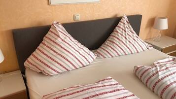 A neatly made bed with striped pillows and a matching blanket, a bedside table with a lamp, and a framed picture on the wall.