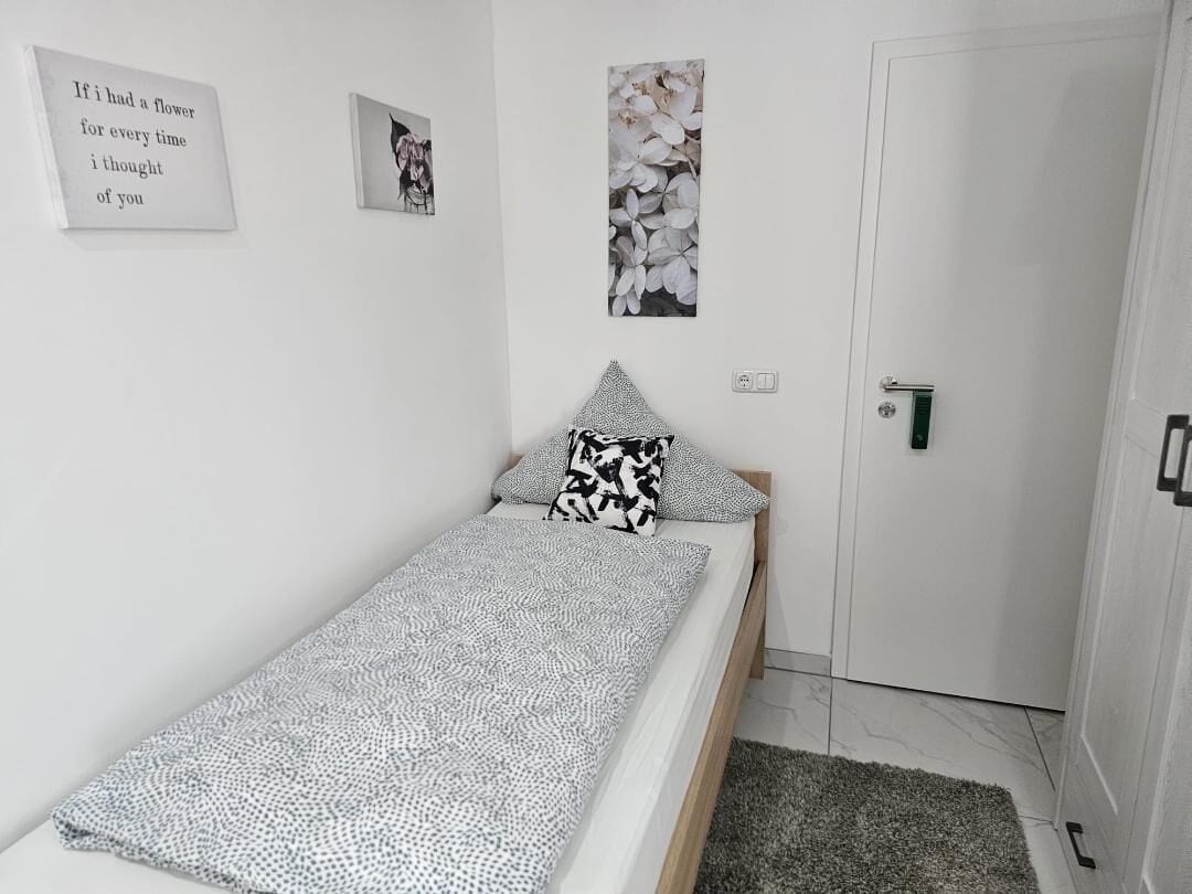 A small, neatly arranged bedroom with a single bed, a door, and two wall-mounted pictures.