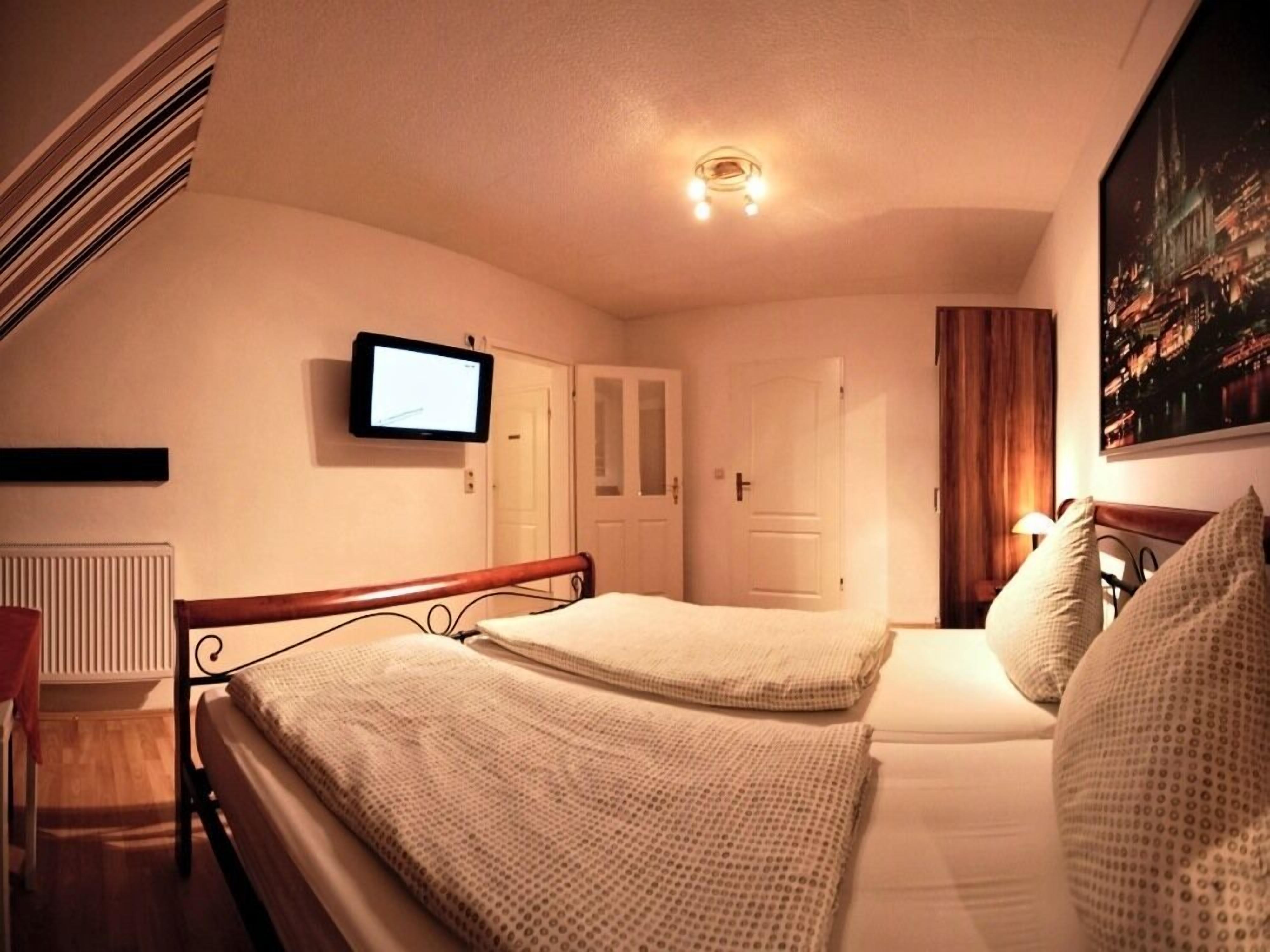 Une chambre d’hôtel avec deux lits, un téléviseur fixé au mur et un tableau représentant un paysage urbain.