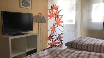 Ein Hotelzimmer mit Fernseher auf einem weißen Schrank, einer Lampe, einem Bett mit gestreifter Bettwäsche und einer Wand mit einem Blattmuster.