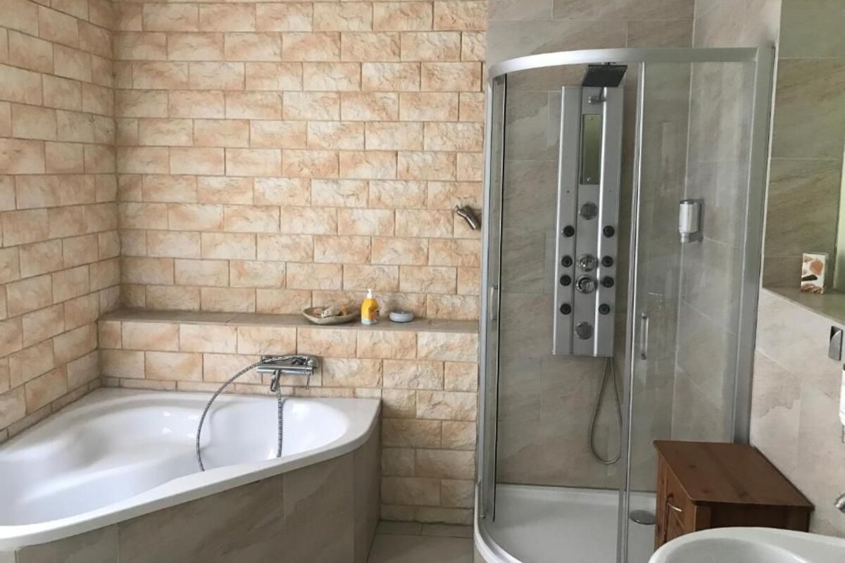 A bathroom with a bathtub, a shower enclosure, and a small wooden cabinet.