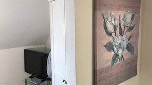 Et værelse med et fjernsyn på et stativ, en dør og en væg med et blomsterbillede.