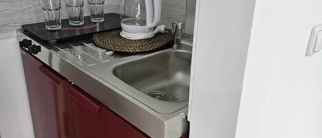 A compact kitchen with a sink, a kettle, and three glasses on the counter.
