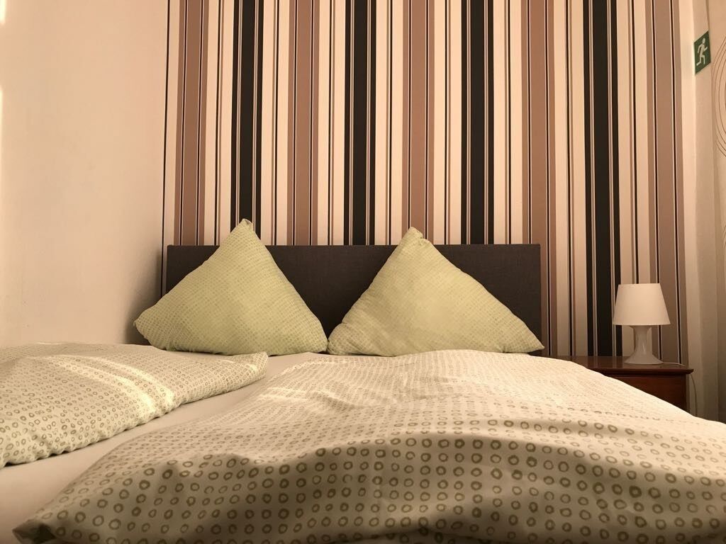 Un lit avec un mur à rayures derrière, une table de chevet avec une lampe et un panneau vert sur le mur.