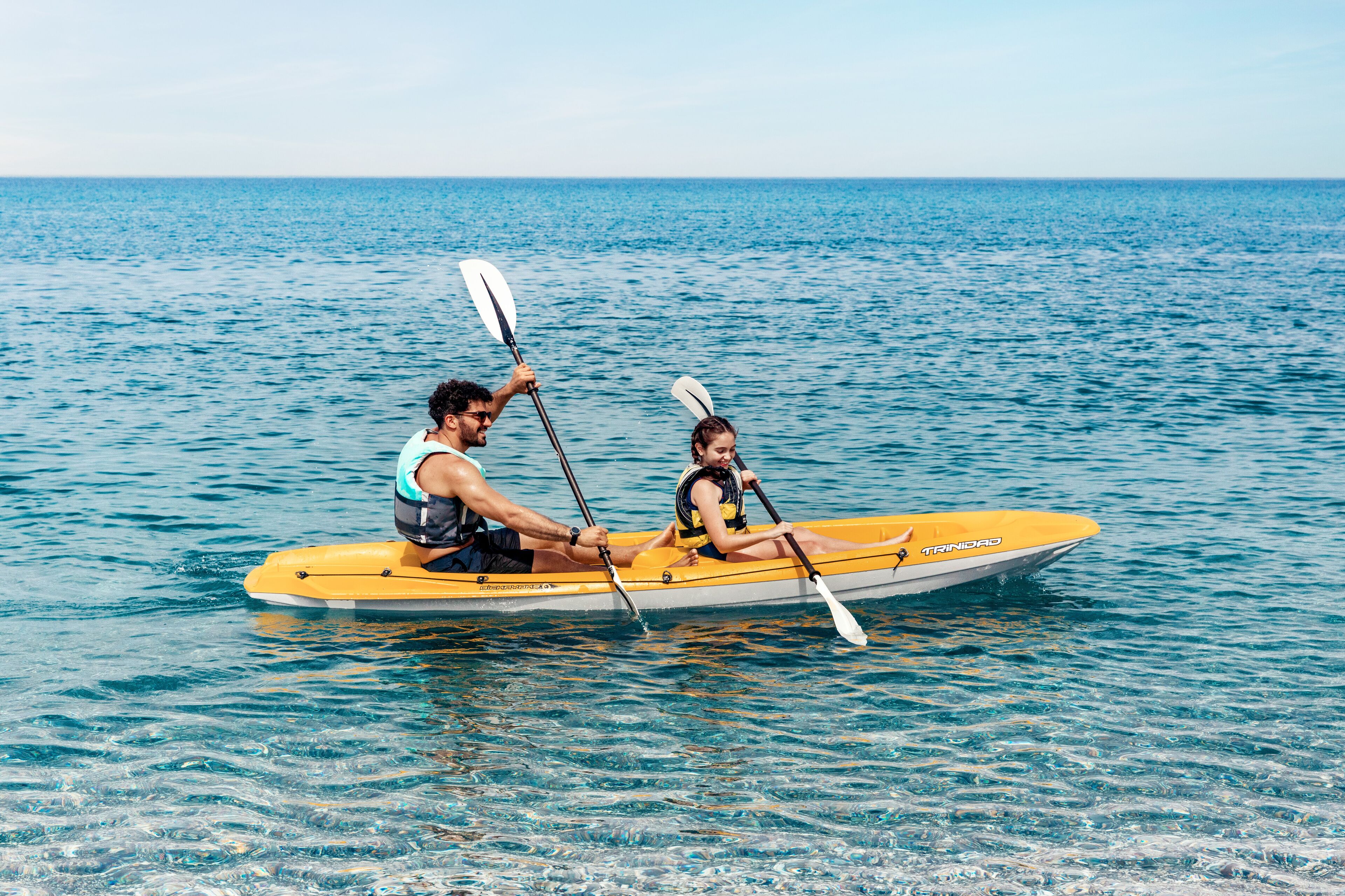 Un couple dans un kayak jaune, sur une mer calme.