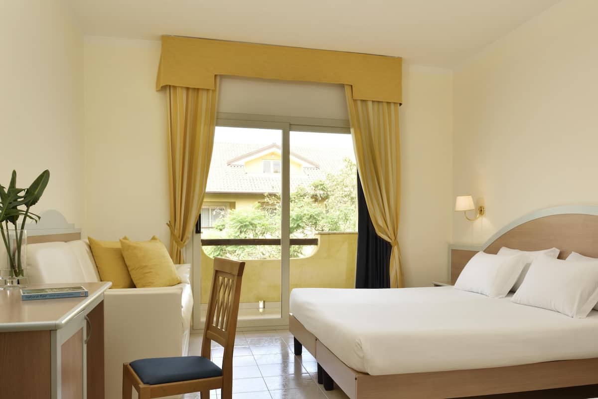A hotel room with a bed, a desk, a chair, and a window with curtains.