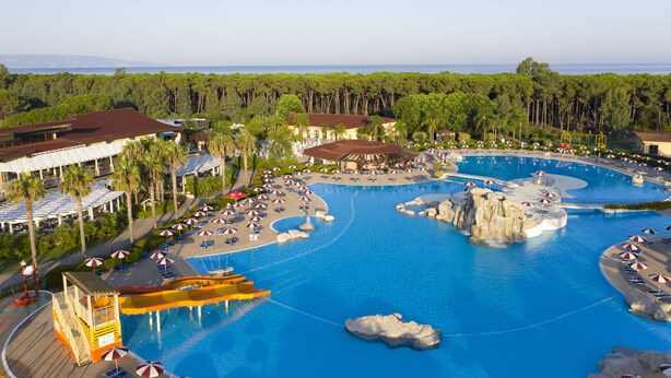 Un resort con una gran piscina, palmeras y vista al océano.